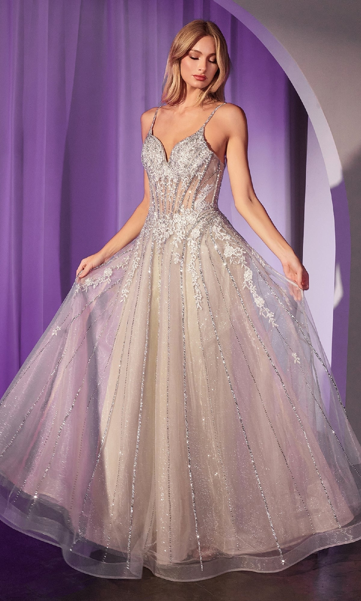 A woman poses in front of a purple-lit backdrop wearing the Ladivine CD786, a floor-length Crystal-Beaded Long Prom Dress with a fitted bodice and sheer panels.